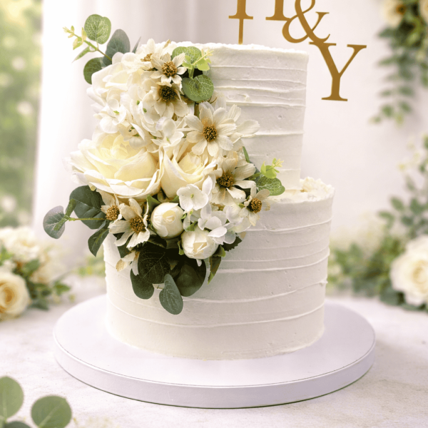 Two tier white buttercream wedding cake with floral cascade and gold H&Y topper, handcrafted by RF Bakery Bolton